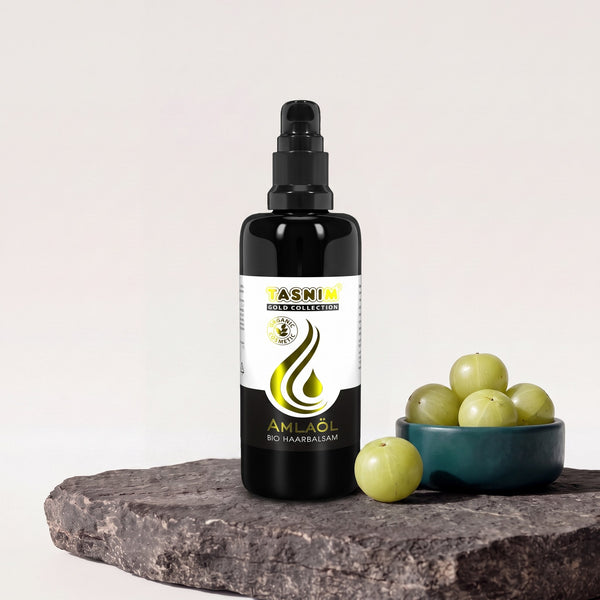 Tasnim Amlaöl Haarbalsam, 100-ml-Pumpflasche auf Basaltplatte, daneben eine Petrol-Schale mit frischen Amla-Früchten