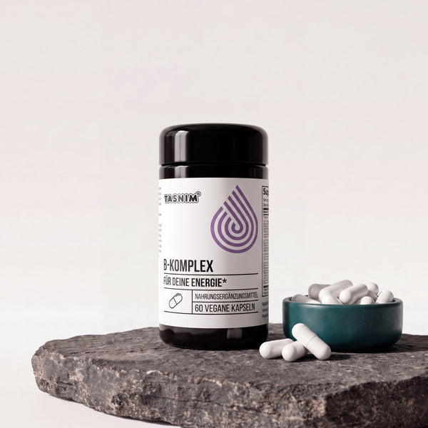 Tasnim Vitamin B-Komplex, Dose mit 60 veganen Kapseln auf Basaltplatte, daneben eine Petrol-Schale mit weißen Kapseln