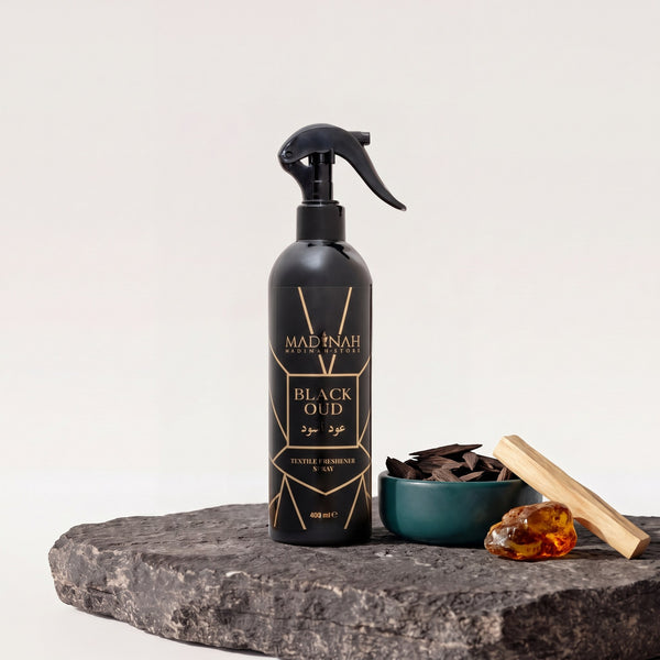 Textilerfrischer Black Oud, 400-ml-Sprühflasche auf dunkler Steinplatte, daneben eine Petrol-Schale mit Oud-Holz, Sandelholz und Amberharz