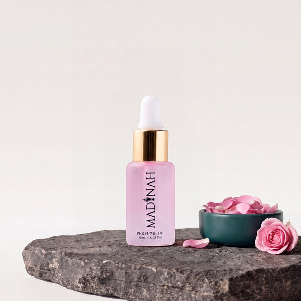 Rose Parfümöl, 10-ml-Flakon mit Pipette und rosafarbener Füllung auf dunkler Steinplatte, daneben eine Petrol-Schale mit rosa Rosenblättern und einer Rose