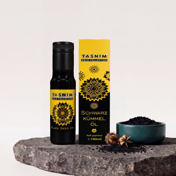 Tasnim Schwarzkümmelöl Gold Collection 100 ml, Flasche und gelb-schwarze Geschenkbox auf Basaltplatte mit Petrol-Schale