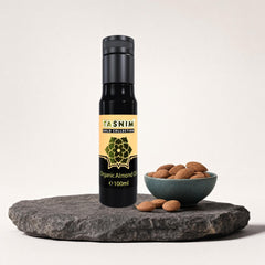 Tasnim Gold Collection Organic Almond Oil 100 ml auf dunkler Steinplatte, daneben eine Petrol-Schale mit Mandeln