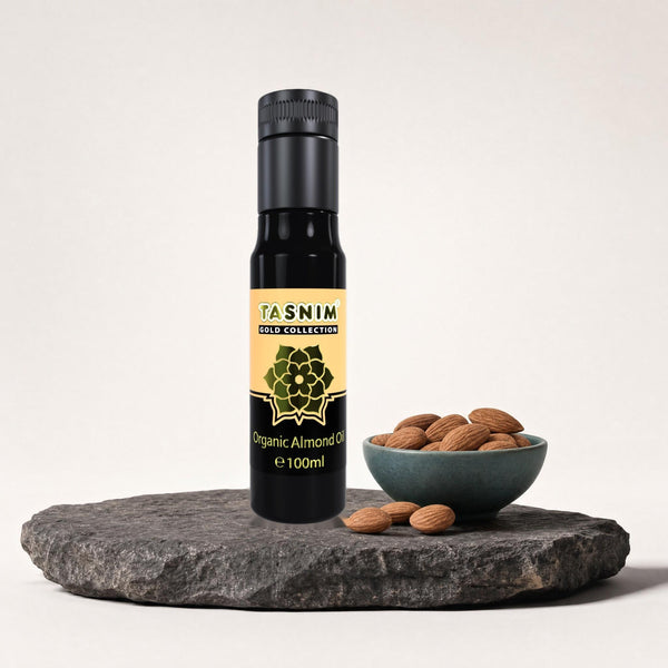 Tasnim Gold Collection Organic Almond Oil 100 ml auf dunkler Steinplatte, daneben eine Petrol-Schale mit Mandeln