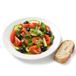 Verwendungsanlass: einfacher Tomaten-Gurken-Salat mit Oliven und Basilikum auf einem weißen Teller, mit Olivenöl beträufelt, daneben eine Scheibe Weißbrot, vor reinweißem Hintergrund.