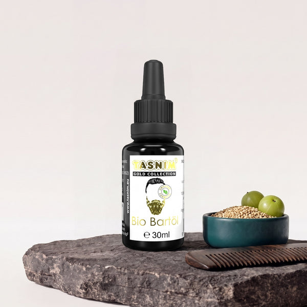 Tasnim Gold Collection Bartöl 30 ml, Pipettenflasche auf Basaltplatte, daneben eine Petrol-Schale mit Sesam und Amla-Früchten und ein Bartkamm aus Holz