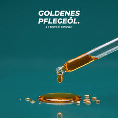 Textur: ein goldener Tropfen Bartöl fällt aus der Glaspipette in eine kleine Ölpfütze mit Sesamsamen