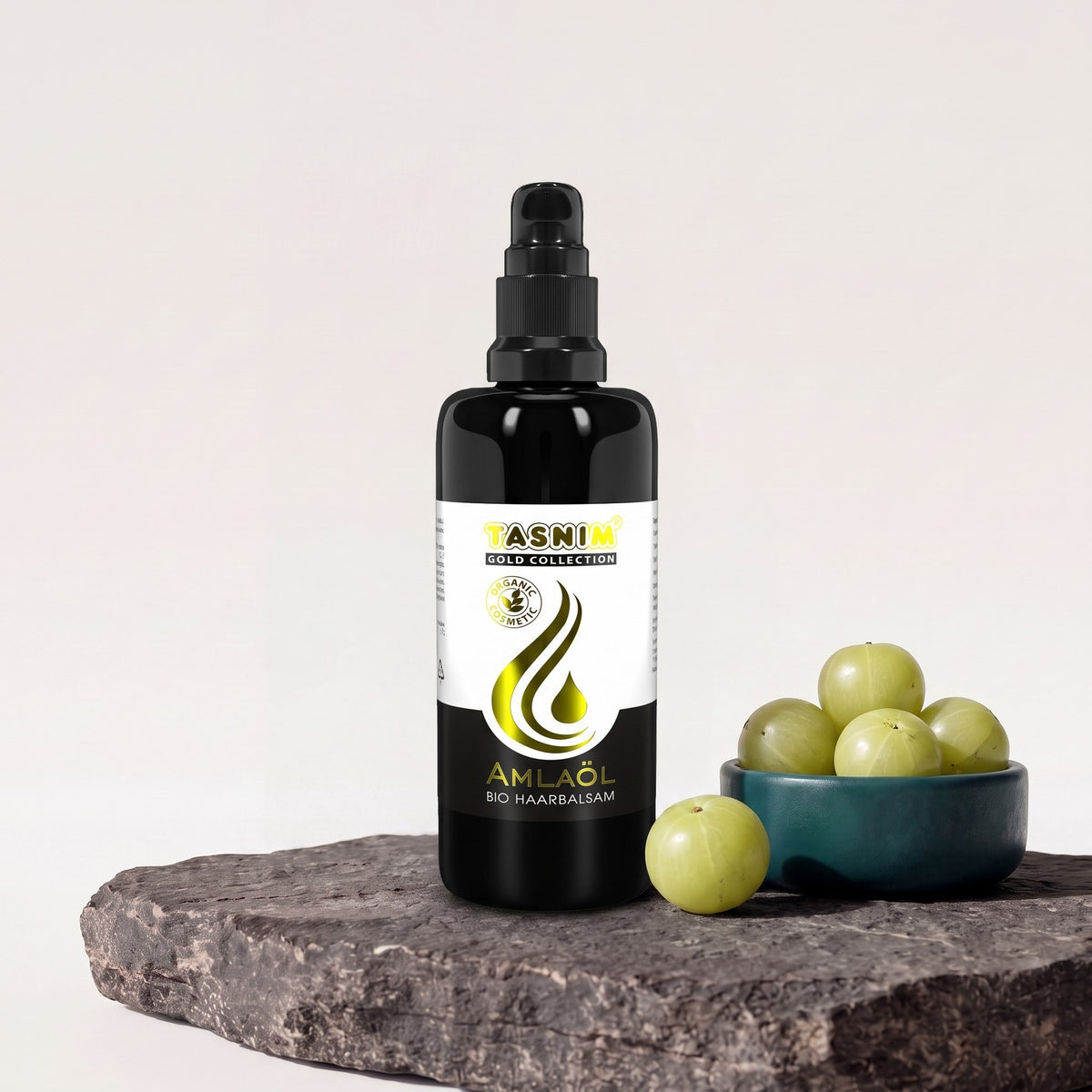Tasnim Amlaöl Haarbalsam, 100-ml-Pumpflasche auf Basaltplatte, daneben eine Petrol-Schale mit frischen Amla-Früchten