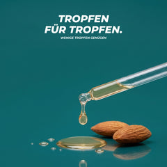 Textur: ein Tropfen Bittermandelöl fällt aus der Glaspipette in eine kleine Ölpfütze neben zwei Mandeln