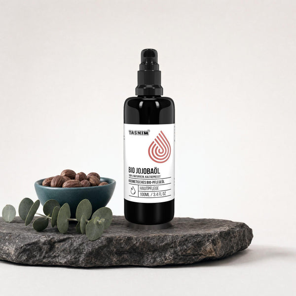 Tasnim Jojobaöl 100 ml mit Pumpspender auf Basaltplatte, daneben eine Petrol-Schale mit Jojobasamen