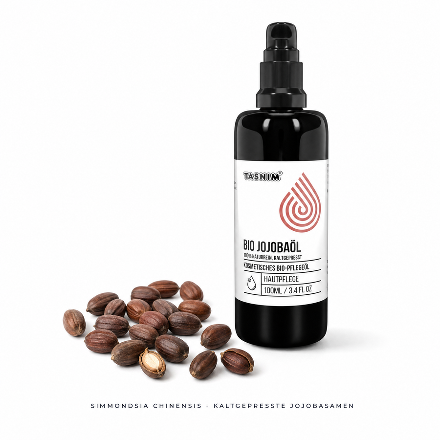 Schwarze 100-ml-Flasche Tasnim Bio Jojobaöl mit Pumpspender und weißem Etikett neben losen braunen Jojobasamen auf weißem Hintergrund, Bildunterschrift „Simmondsia chinensis – kaltgepresste Jojobasamen“.