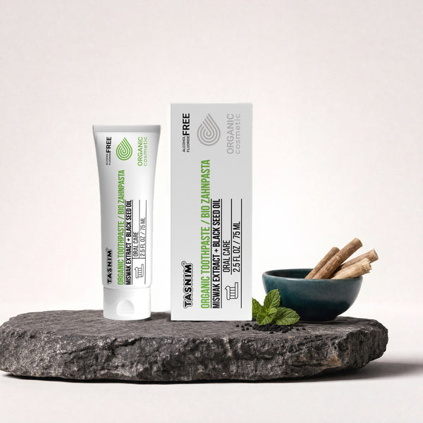 Tasnim Bio-Zahnpasta 75 ml, Tube und Faltschachtel auf Schieferplatte mit Petrol-Schale, Miswak-Stäbchen und Minze