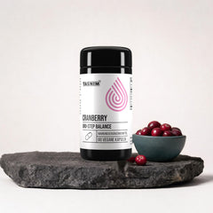 Tasnim Cranberry Uro-Step Balance, Dose mit 60 veganen Kapseln auf dunkler Steinplatte, daneben eine Petrol-Schale mit frischen Cranberries