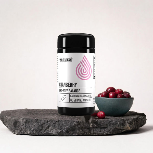 Tasnim Cranberry Uro-Step Balance, Dose mit 60 veganen Kapseln auf dunkler Steinplatte, daneben eine Petrol-Schale mit frischen Cranberries