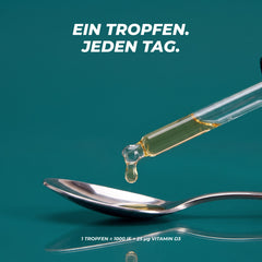 Ein goldener Tropfen fällt aus der Glaspipette auf einen Löffel – 1 Tropfen entspricht 1000 IE bzw. 25 µg Vitamin D3
