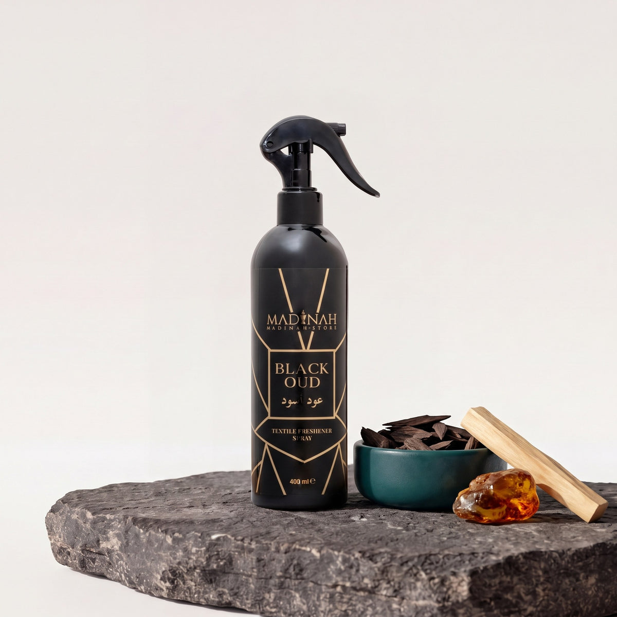 Textilerfrischer Black Oud, 400-ml-Sprühflasche auf dunkler Steinplatte, daneben eine Petrol-Schale mit Oud-Holz, Sandelholz und Amberharz