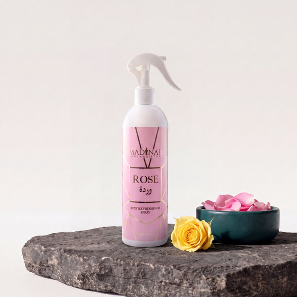 Textilerfrischer Rose, 400-ml-Sprühflasche auf dunkler Steinplatte, daneben eine Petrol-Schale mit Rosenblätter und eine gelbe Rose