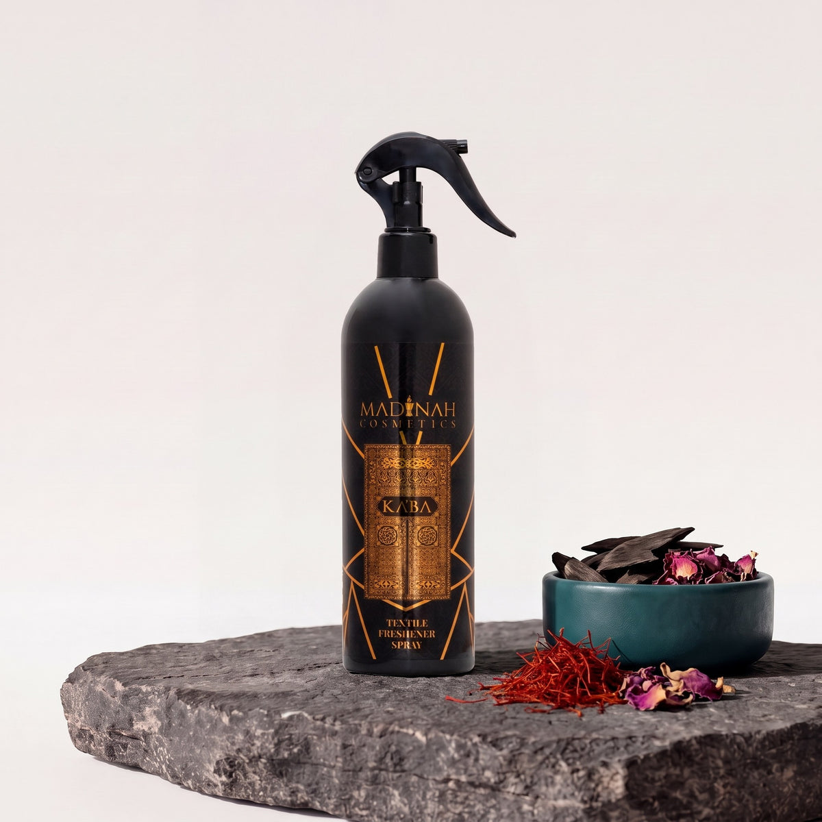 Textilerfrischer Ka'ba, 400-ml-Sprühflasche auf dunkler Steinplatte, daneben eine Petrol-Schale mit Oud-Holz, Safran und Rosenblätter