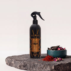 Textilerfrischer Ka'ba, 400-ml-Sprühflasche auf dunkler Steinplatte, daneben eine Petrol-Schale mit Oud-Holz, Safran und Rosenblätter