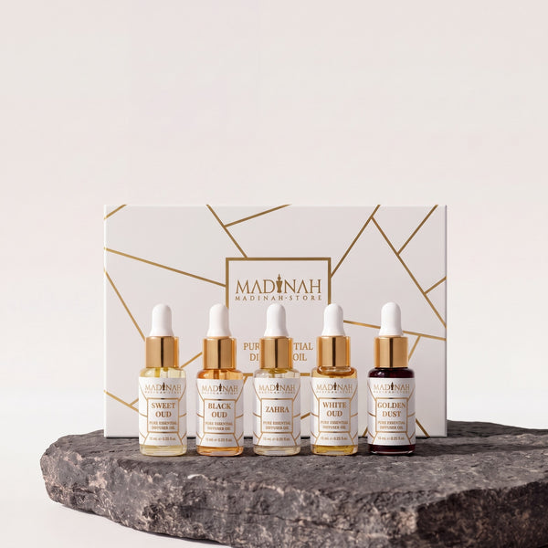 Duftöl 5er Set NR. 2: weiße Geschenkbox mit Goldlinien und fünf 10-ml-Pipettenfläschchen (Sweet Oud, Black Oud, Zahra, White Oud, Golden Dust) auf dunkler Steinplatte