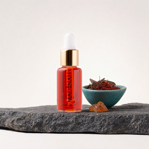 Ka'ba Parfümöl, 10-ml-Flakon mit Pipette und roter Füllung auf dunkler Steinplatte, daneben eine Petrol-Schale mit Oud-Holz, Safranfäden und getrockneten Rosenblüten